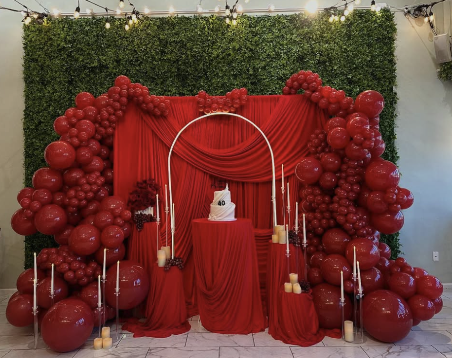Red balloon installation framing a birthday cake and draped backdrop