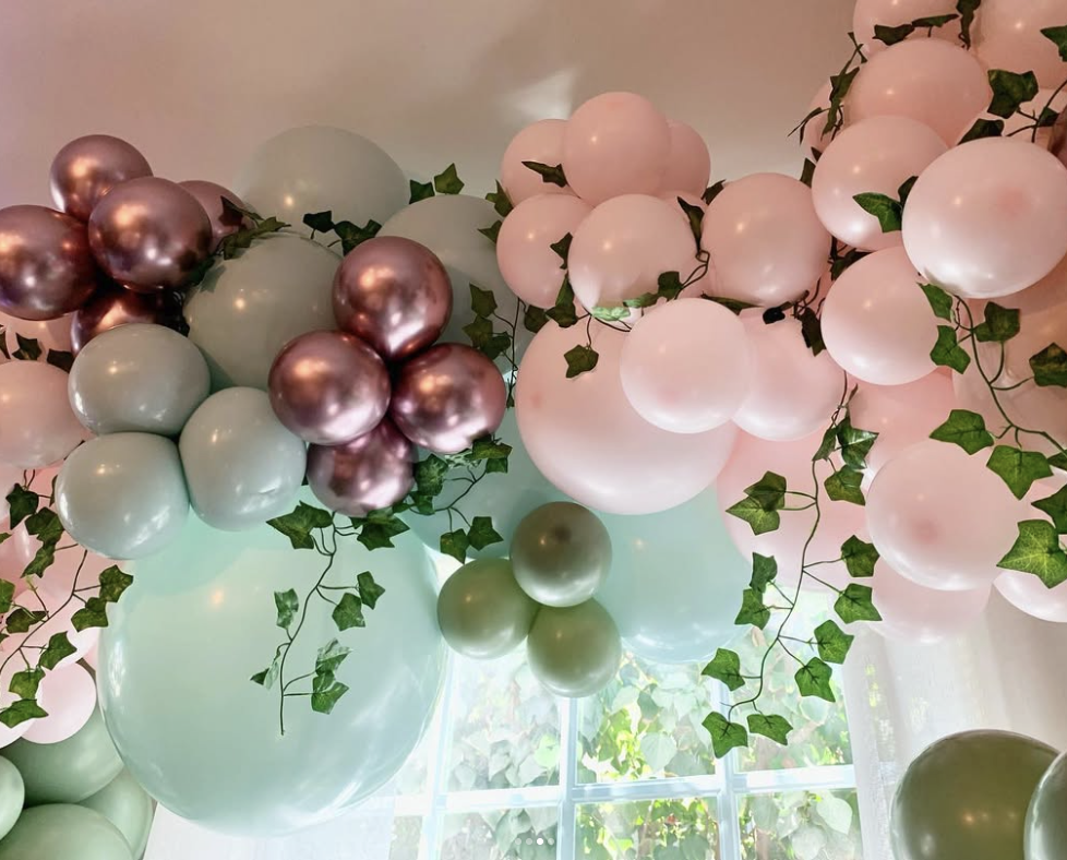 Pink, sage, and metallic balloons arranged in an arch around a window